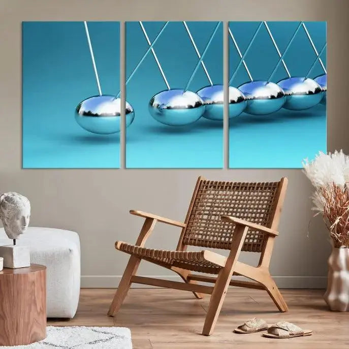 The Wall Art Newton's Cradle Canvas Print is displayed as a triptych on a teal background. Each piece is gallery-wrapped and crafted on museum-quality canvases with a UV-protective coating, ensuring lasting vibrancy and protection.