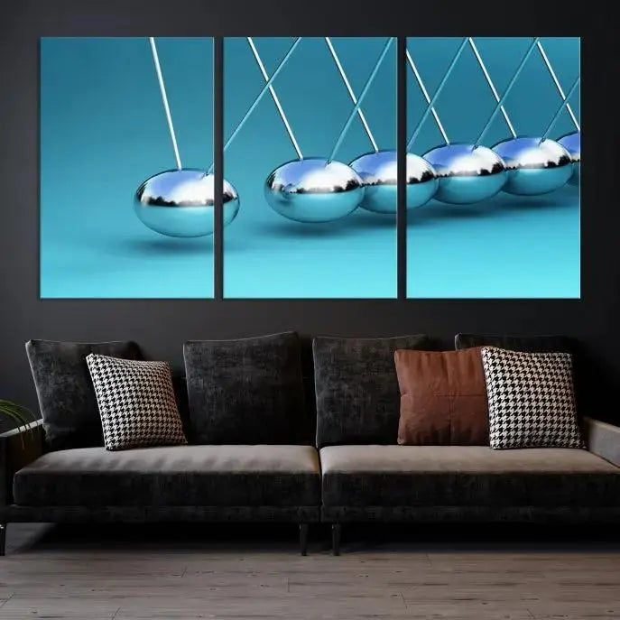 The Wall Art Newton's Cradle Canvas Print is displayed as a triptych on a teal background. Each piece is gallery-wrapped and crafted on museum-quality canvases with a UV-protective coating, ensuring lasting vibrancy and protection.