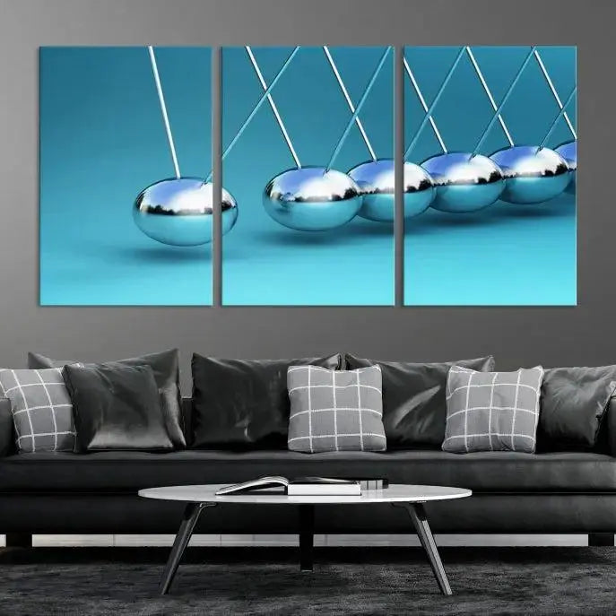 The Wall Art Newton's Cradle Canvas Print is displayed as a triptych on a teal background. Each piece is gallery-wrapped and crafted on museum-quality canvases with a UV-protective coating, ensuring lasting vibrancy and protection.