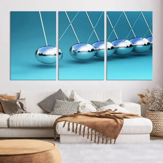 The Wall Art Newton's Cradle Canvas Print is displayed as a triptych on a teal background. Each piece is gallery-wrapped and crafted on museum-quality canvases with a UV-protective coating, ensuring lasting vibrancy and protection.