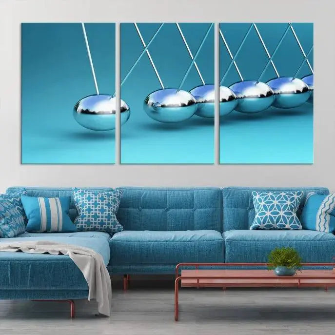 The Wall Art Newton's Cradle Canvas Print is displayed as a triptych on a teal background. Each piece is gallery-wrapped and crafted on museum-quality canvases with a UV-protective coating, ensuring lasting vibrancy and protection.