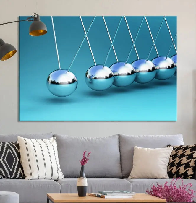 The Wall Art Newton's Cradle Canvas Print is displayed as a triptych on a teal background. Each piece is gallery-wrapped and crafted on museum-quality canvases with a UV-protective coating, ensuring lasting vibrancy and protection.