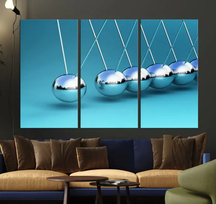 The Wall Art Newton's Cradle Canvas Print is displayed as a triptych on a teal background. Each piece is gallery-wrapped and crafted on museum-quality canvases with a UV-protective coating, ensuring lasting vibrancy and protection.