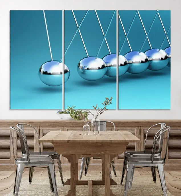 The Wall Art Newton's Cradle Canvas Print is displayed as a triptych on a teal background. Each piece is gallery-wrapped and crafted on museum-quality canvases with a UV-protective coating, ensuring lasting vibrancy and protection.