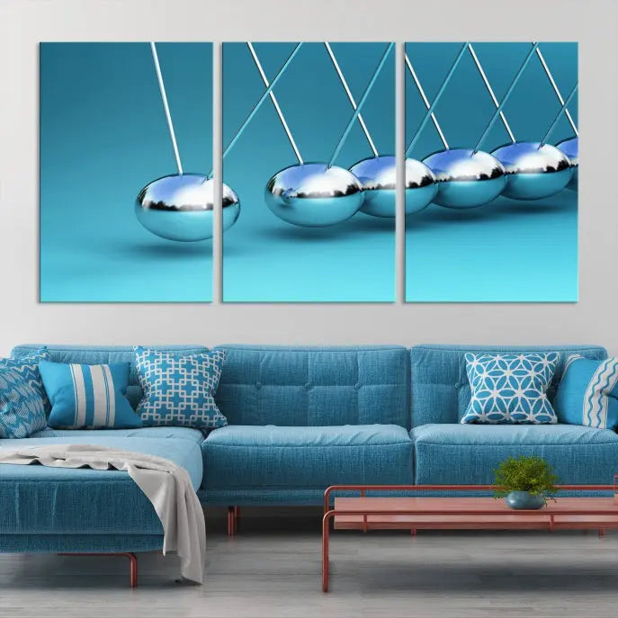 The Wall Art Newton's Cradle Canvas Print is displayed as a triptych on a teal background. Each piece is gallery-wrapped and crafted on museum-quality canvases with a UV-protective coating, ensuring lasting vibrancy and protection.