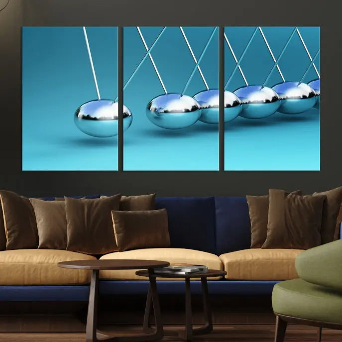 The Wall Art Newton's Cradle Canvas Print is displayed as a triptych on a teal background. Each piece is gallery-wrapped and crafted on museum-quality canvases with a UV-protective coating, ensuring lasting vibrancy and protection.