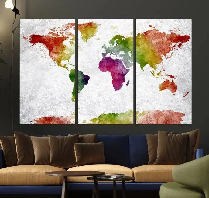 The Watercolor World Map Wall Art Canvas Print, a triptych printed on museum-quality canvases with UV-protective coating, hangs elegantly in a modern living room setting. Ready to hang, it adds an elegant touch to your space.