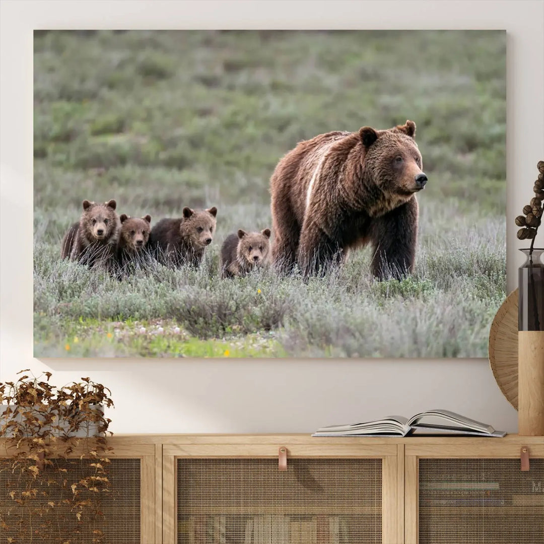 The canvas wall art print, titled "Queen of the Tetons," features a photo of 399 grizzly bear cubs walking with a larger bear in a green, open field. This striking piece is framed and leaning against a wall, showcasing its gallery-quality finish.