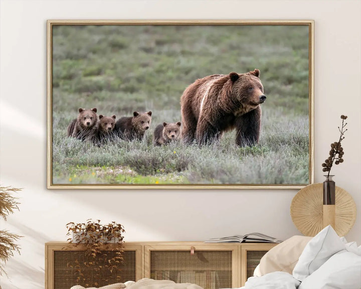 The canvas wall art print, titled "Queen of the Tetons," features a photo of 399 grizzly bear cubs walking with a larger bear in a green, open field. This striking piece is framed and leaning against a wall, showcasing its gallery-quality finish.