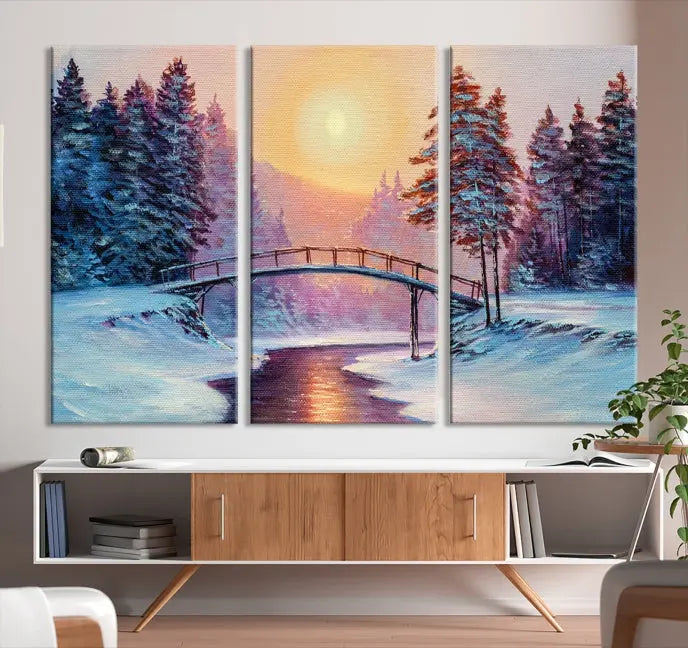 The "Winter Bridge Painting Wall Art Landscape Canvas Print" captures a serene winter landscape across three panels, showcasing a bridge, snowy trees, and a setting sun on museum-quality canvases. Each piece is gallery wrapped for an elegant finish that enhances the tranquility of the scene.