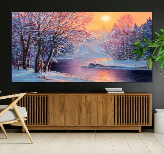 In a cozy living room, you'll find wall art titled "Winter Landscape Painting Wall Art Canvas Print," showcasing a serene snowy river scene at sunset on a museum-quality canvas with gallery-wrapped edges.