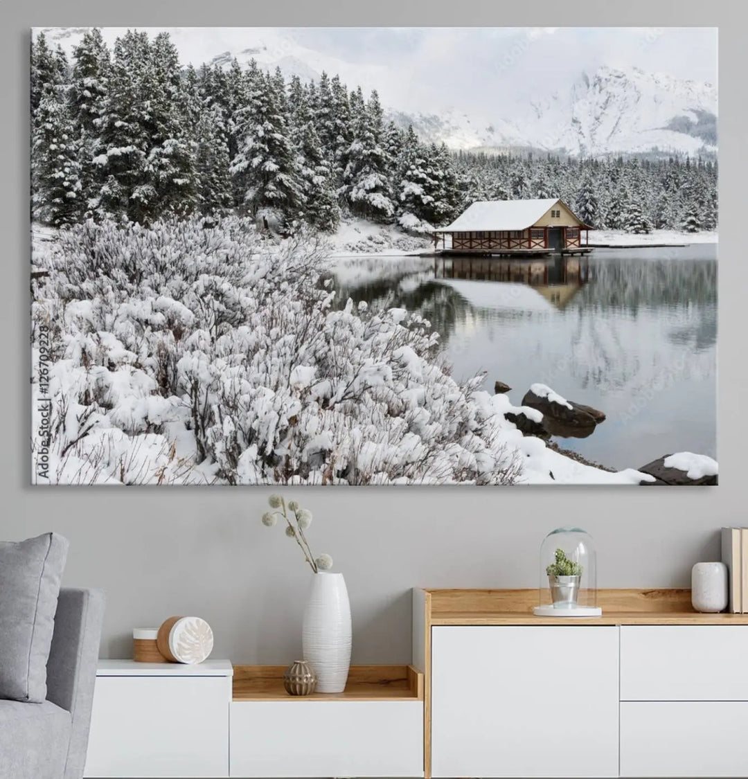 Experience the beauty of winter with the "Cabin by the Lake Canvas Wall Art," showcasing a serene snowy landscape. This rustic nature decor features a cozy cabin nestled amid snow-laden trees, set against a breathtaking mountain view, perfect for enhancing your living room.