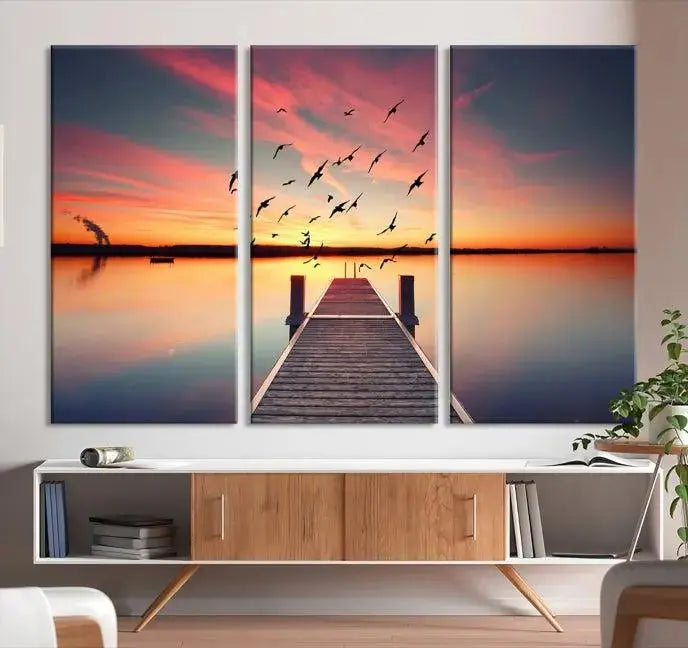 The Wood Bridge and Sunset Wall Art Canvas Print showcases a tranquil sunset scene featuring a wooden dock, soaring birds, and a vibrant sky. It comes ready to hang.