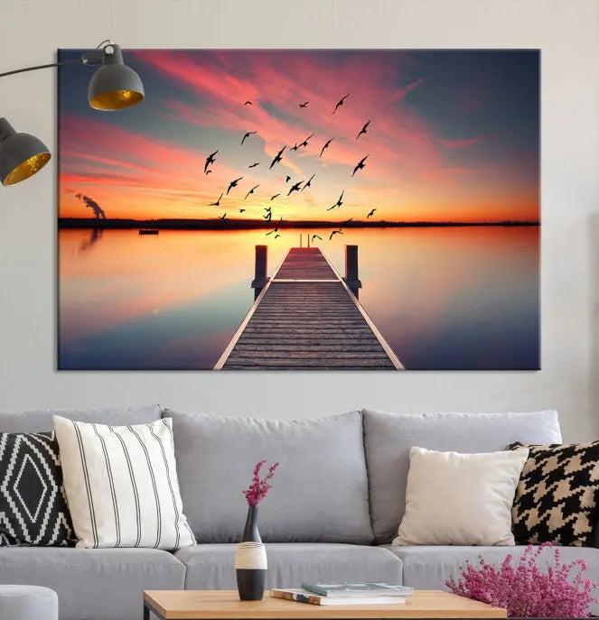 The Wood Bridge and Sunset Wall Art Canvas Print showcases a tranquil sunset scene featuring a wooden dock, soaring birds, and a vibrant sky. It comes ready to hang.