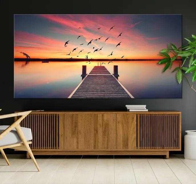 The Wood Bridge and Sunset Wall Art Canvas Print showcases a tranquil sunset scene featuring a wooden dock, soaring birds, and a vibrant sky. It comes ready to hang.