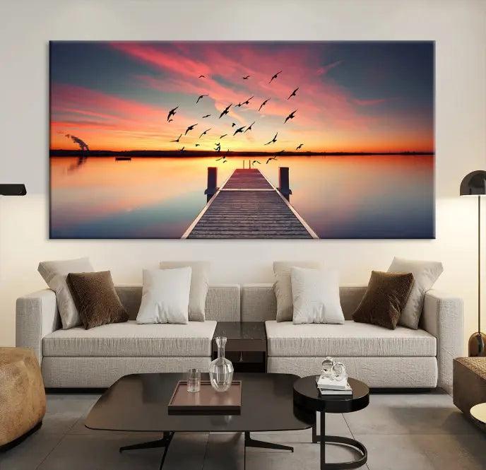 The Wood Bridge and Sunset Wall Art Canvas Print showcases a tranquil sunset scene featuring a wooden dock, soaring birds, and a vibrant sky. It comes ready to hang.