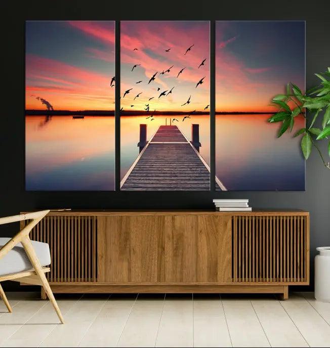 The Wood Bridge and Sunset Wall Art Canvas Print showcases a tranquil sunset scene featuring a wooden dock, soaring birds, and a vibrant sky. It comes ready to hang.