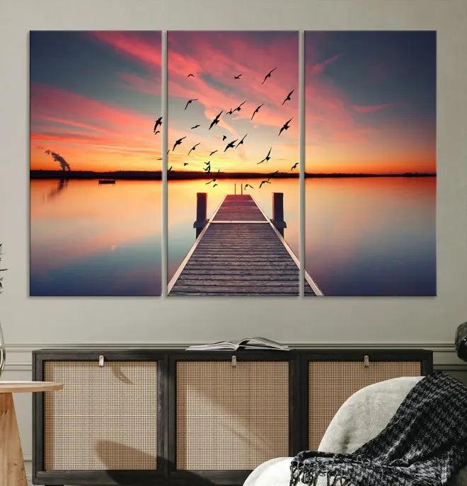 The Wood Bridge and Sunset Wall Art Canvas Print showcases a tranquil sunset scene featuring a wooden dock, soaring birds, and a vibrant sky. It comes ready to hang.