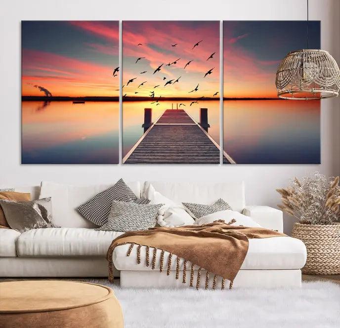 The Wood Bridge and Sunset Wall Art Canvas Print showcases a tranquil sunset scene featuring a wooden dock, soaring birds, and a vibrant sky. It comes ready to hang.