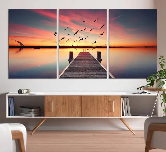 The Wood Bridge and Sunset Wall Art Canvas Print showcases a tranquil sunset scene featuring a wooden dock, soaring birds, and a vibrant sky. It comes ready to hang.