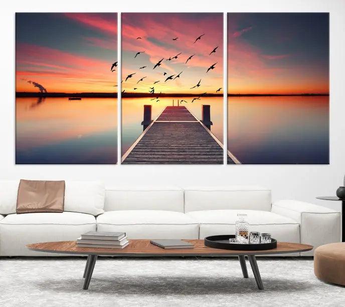 The Wood Bridge and Sunset Wall Art Canvas Print showcases a tranquil sunset scene featuring a wooden dock, soaring birds, and a vibrant sky. It comes ready to hang.