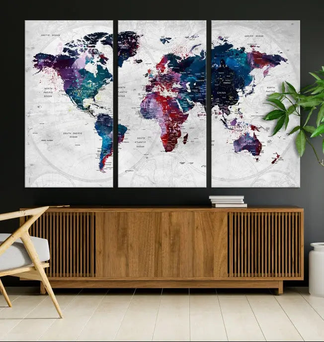 The "World Map Wall Art Watercolor Wall Art Canvas Print," a triptych featuring a vibrant world map, is gallery wrapped on museum-quality canvas and enhances the dark wall.