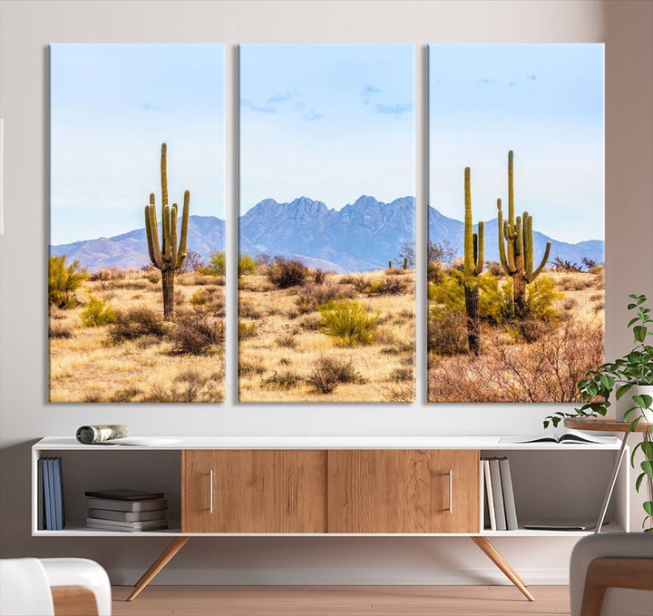 The Arizona Desert Cactus Wall Art Canvas Print, positioned above the console in a modern room, showcases a triptych desert landscape featuring cacti and mountains. Crafted on museum-quality polycotton canvas, it is finished with gallery-wrapped edges and an advanced UV-protective coating.