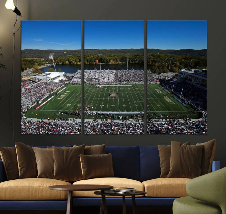 The Army Black Knights Football Team Print on West Point Michie Stadium is showcased with an aerial view capturing a lively football stadium surrounded by lush trees and a river. This wall art is printed on museum-quality canvas and mounted on a stretched wood frame.