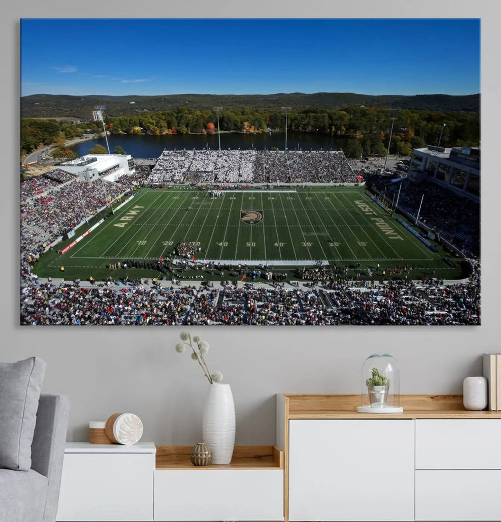 The Army Black Knights Football Team Print on West Point Michie Stadium is showcased with an aerial view capturing a lively football stadium surrounded by lush trees and a river. This wall art is printed on museum-quality canvas and mounted on a stretched wood frame.