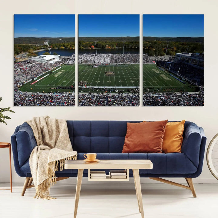 The Army Black Knights Football Team Print on West Point Michie Stadium is showcased with an aerial view capturing a lively football stadium surrounded by lush trees and a river. This wall art is printed on museum-quality canvas and mounted on a stretched wood frame.