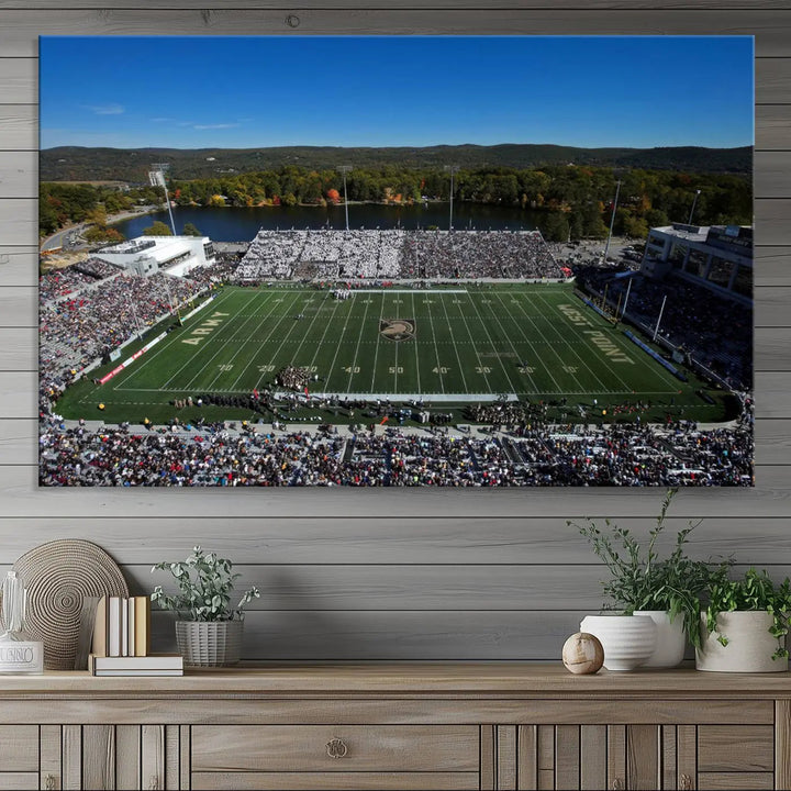 The Army Black Knights Football Team Print on West Point Michie Stadium is showcased with an aerial view capturing a lively football stadium surrounded by lush trees and a river. This wall art is printed on museum-quality canvas and mounted on a stretched wood frame.