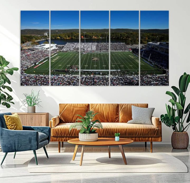 The Army Black Knights Football Team Print on West Point Michie Stadium is showcased with an aerial view capturing a lively football stadium surrounded by lush trees and a river. This wall art is printed on museum-quality canvas and mounted on a stretched wood frame.