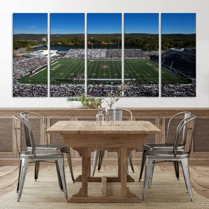 The Army Black Knights Football Team Print on West Point Michie Stadium is showcased with an aerial view capturing a lively football stadium surrounded by lush trees and a river. This wall art is printed on museum-quality canvas and mounted on a stretched wood frame.