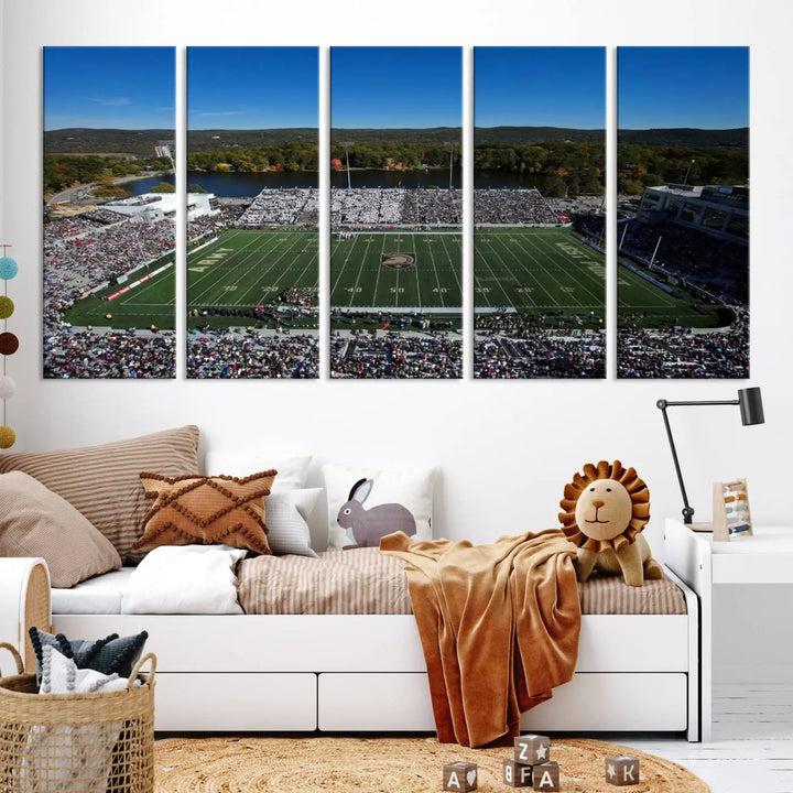 The Army Black Knights Football Team Print on West Point Michie Stadium is showcased with an aerial view capturing a lively football stadium surrounded by lush trees and a river. This wall art is printed on museum-quality canvas and mounted on a stretched wood frame.