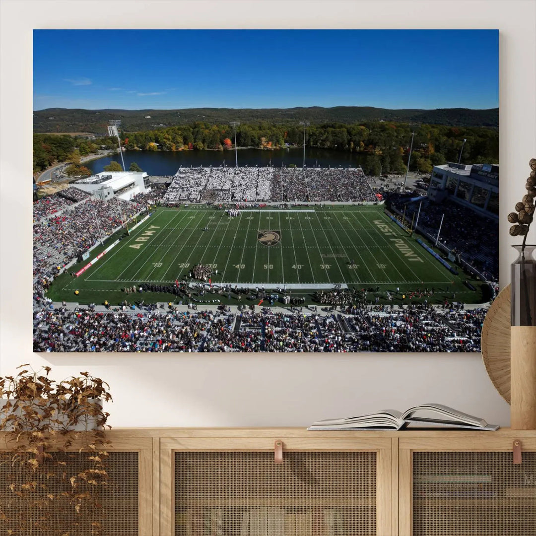 The Army Black Knights Football Team Print on West Point Michie Stadium is showcased with an aerial view capturing a lively football stadium surrounded by lush trees and a river. This wall art is printed on museum-quality canvas and mounted on a stretched wood frame.