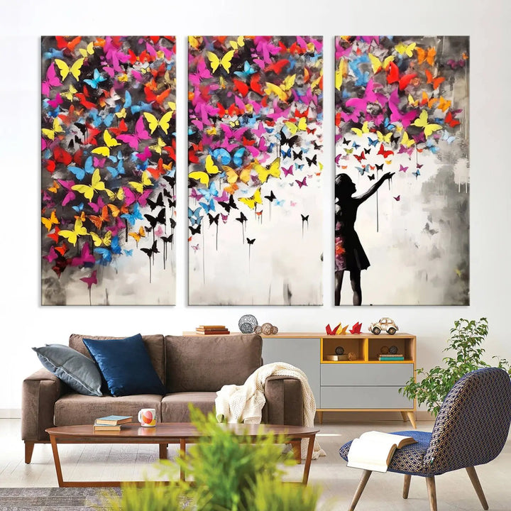 The Banksy Style Wall Art - Girl and Butterfly Explosion features a silhouette of a girl reaching for colorful butterflies on a three-panel canvas print.