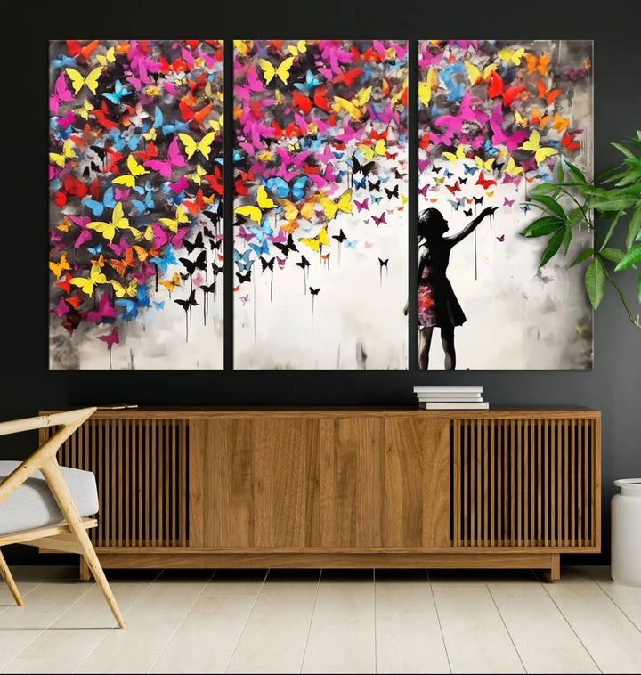 The Banksy Style Wall Art - Girl and Butterfly Explosion features a silhouette of a girl reaching for colorful butterflies on a three-panel canvas print.