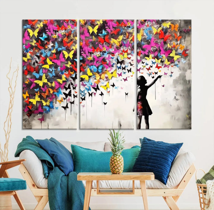 The Banksy Style Wall Art - Girl and Butterfly Explosion features a silhouette of a girl reaching for colorful butterflies on a three-panel canvas print.