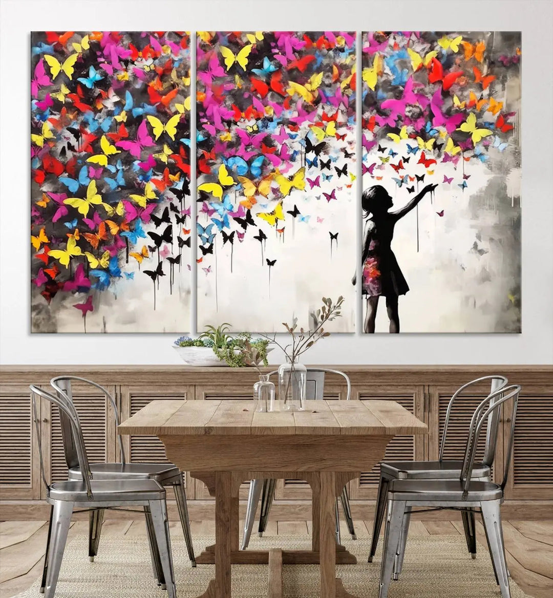 The Banksy Style Wall Art - Girl and Butterfly Explosion features a silhouette of a girl reaching for colorful butterflies on a three-panel canvas print.