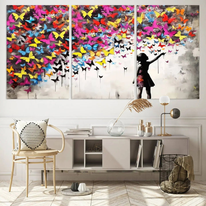 The Banksy Style Wall Art - Girl and Butterfly Explosion features a silhouette of a girl reaching for colorful butterflies on a three-panel canvas print.