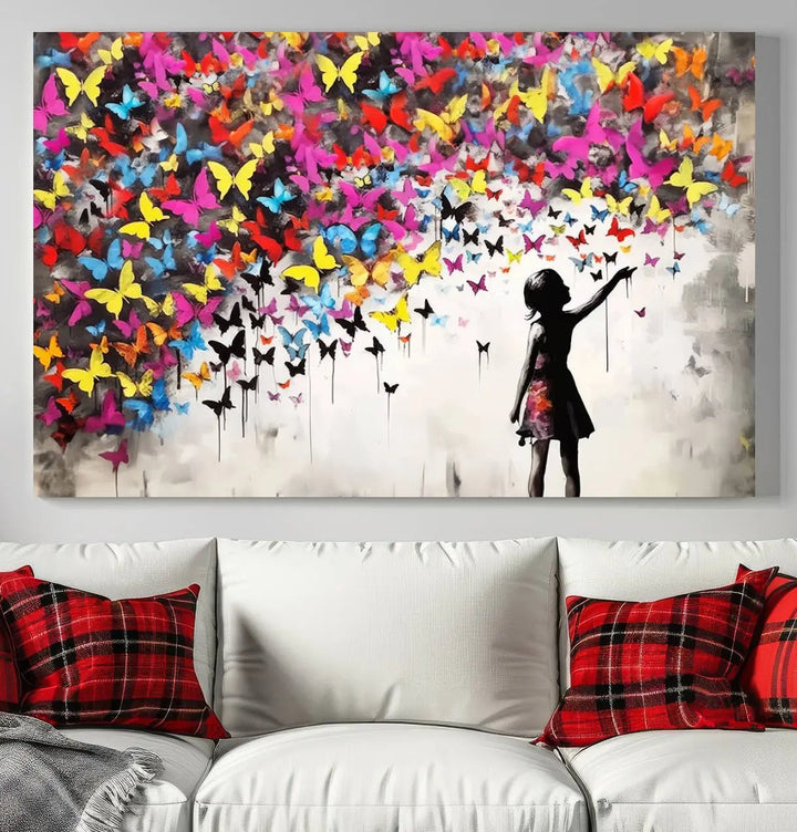 The Banksy Style Wall Art - Girl and Butterfly Explosion features a silhouette of a girl reaching for colorful butterflies on a three-panel canvas print.