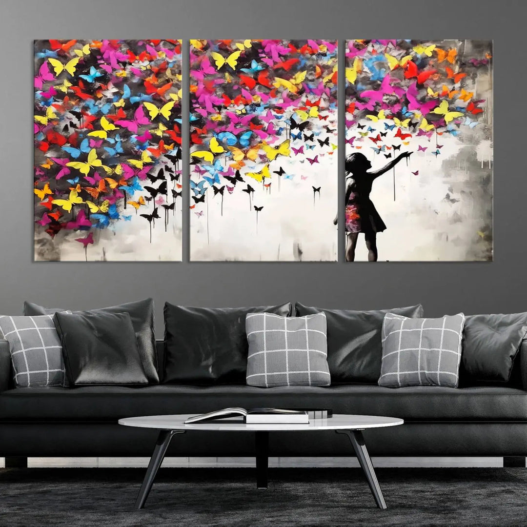 The Banksy Style Wall Art - Girl and Butterfly Explosion features a silhouette of a girl reaching for colorful butterflies on a three-panel canvas print.