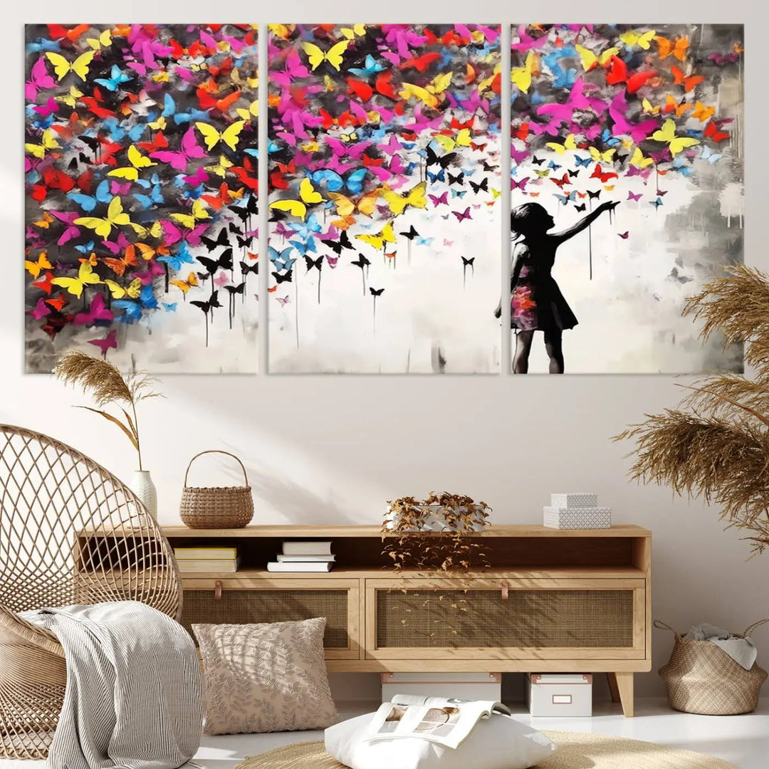 The Banksy Style Wall Art - Girl and Butterfly Explosion features a silhouette of a girl reaching for colorful butterflies on a three-panel canvas print.