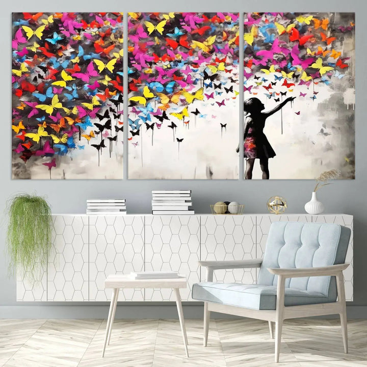 The Banksy Style Wall Art - Girl and Butterfly Explosion features a silhouette of a girl reaching for colorful butterflies on a three-panel canvas print.