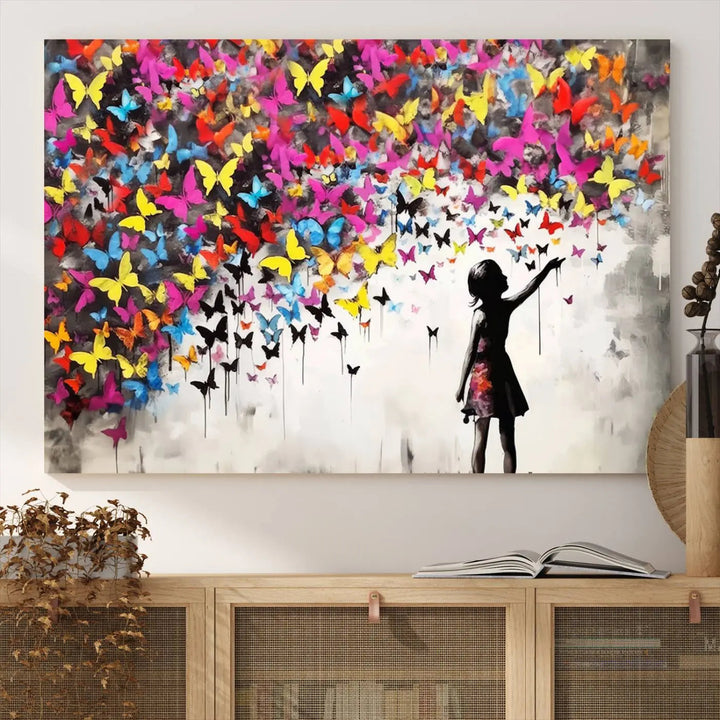 The Banksy Style Wall Art - Girl and Butterfly Explosion features a silhouette of a girl reaching for colorful butterflies on a three-panel canvas print.