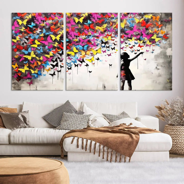 The Banksy Style Wall Art - Girl and Butterfly Explosion features a silhouette of a girl reaching for colorful butterflies on a three-panel canvas print.