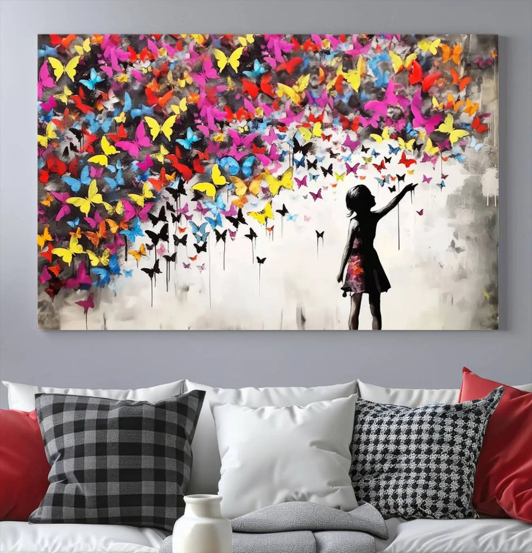 The Banksy Style Wall Art - Girl and Butterfly Explosion features a silhouette of a girl reaching for colorful butterflies on a three-panel canvas print.