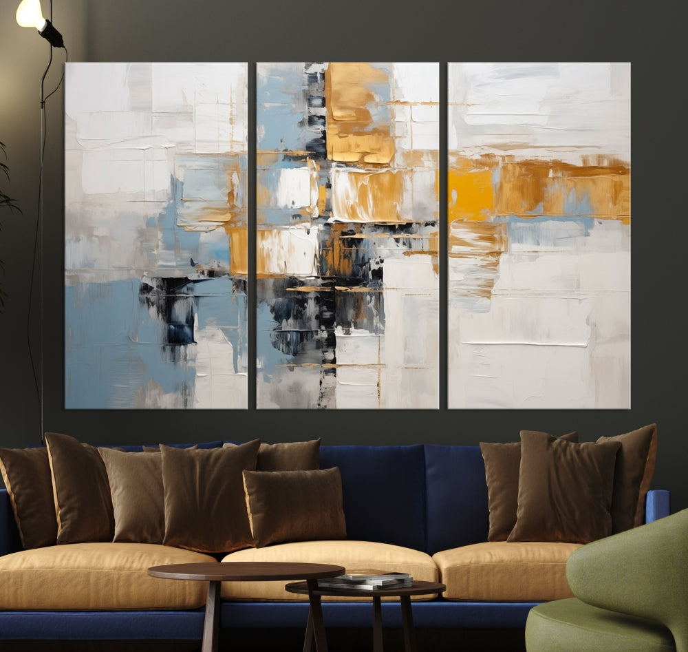 A stunning triptych of the Blue Orange Abstract Wall Art Canvas Print adorns the wall. These gallery-wrapped abstract pieces, showcasing blue, yellow, and white tones, feature a UV-protective coating to maintain their vivid colors.