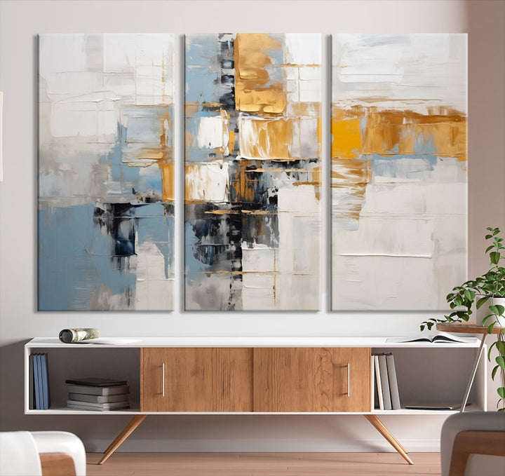 A stunning triptych of the Blue Orange Abstract Wall Art Canvas Print adorns the wall. These gallery-wrapped abstract pieces, showcasing blue, yellow, and white tones, feature a UV-protective coating to maintain their vivid colors.