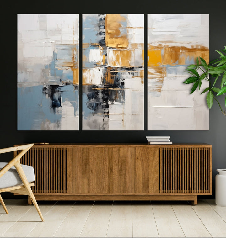 A stunning triptych of the Blue Orange Abstract Wall Art Canvas Print adorns the wall. These gallery-wrapped abstract pieces, showcasing blue, yellow, and white tones, feature a UV-protective coating to maintain their vivid colors.